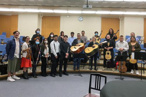 A group of people in a music room with tiered floor, most holding musical instruments, and some in face masks.