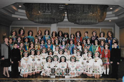 Dance team photo, members in costume posing in symmetrical rows below chandeliers.
