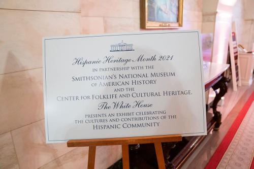 A white sign on a stand reads: Hispanic Heritage Month 2021. In Partnership with the Smithsonian’s National Museum of American History and the Center for Folklife and Cultural Heritage, The White House presents an exhibit celebrating the cultures and cont