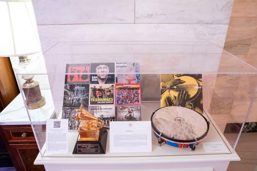 A display case containing a golden GRAMMY Award, collage of album artwork, and a hand drum. Two text cards are too small to read.