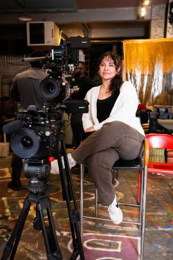 A young woman sits behind a video camera.