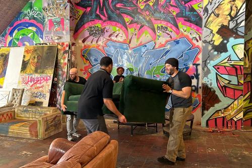 Three people move a green couch in the graffiti-covered room.