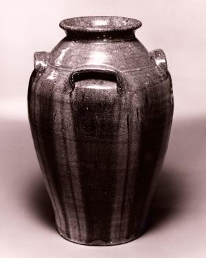 Bulbous dark jug with three visible hand holds below the mouth. It has vertical streaks in a lighter glaze rising from the bottom.