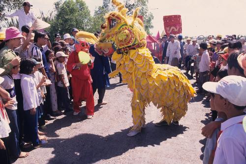 Two people in a yellow lion dance costume perform in front of a crowd of people outdoors.