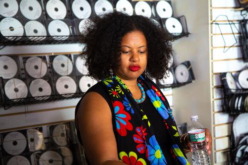 A woman in a floral blouse stands in front of a display of CDs.