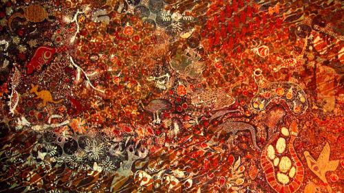 Dyed textile in red and orange tones, printed with geometric patterns and stylized animal figures.