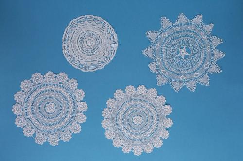 Four intricately woven lacework pieces are arranged in two diagonal rows against a blue background.