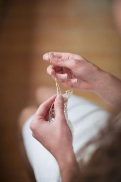 In the center of the image, a woman's hands hold a needle in the midst of making a piece of lacework.