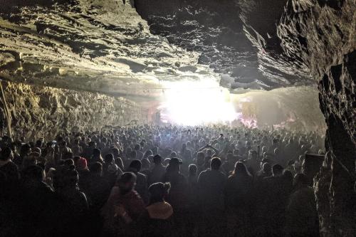 Hundreds of people in a cavern facing a bright white stage.