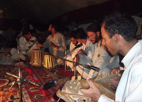 Men sit on carpet with musical instruments and microphones singing together.