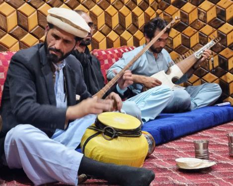 Three men seated on a red carpet play musical instruments together.