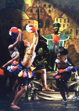 Four dancers on stage, with a backdrop of a hand-drawn village in brown tones.