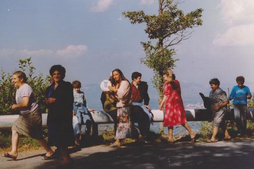 A group of adult women walk in a procession, some holding hand drums. 
