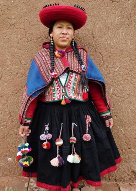 A woman in traditional Peruvian wool dress: black skirt, woven vests and shawl, red wide-brimmed hats all adorned with colorful yarn pom-poms and tassels.