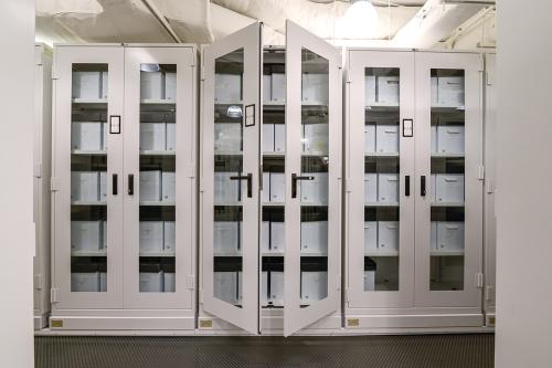 White cabinets with glass doors, partway opened to reveal gray boxes inside.