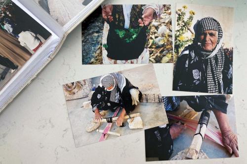 Several color photographs arranged inside and beside a photo album. The only portrait shows an elderly woman in black floral blouse and black and white headscarf. In the other photo, the same woman, presumably, is holding up a plastic bag of green leaves 