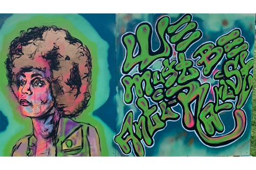 Graffiti mural depicting a woman with an Afro on the left and the words, in script, We Must Be Anti-Racist, on the right.