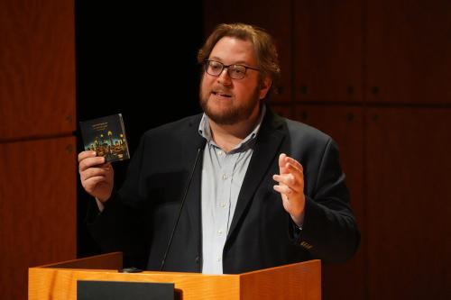 A man holds up a CD, speaking from a podium on stage.