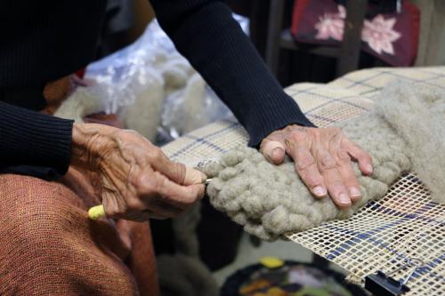 Close-up on a pair of hands as they pull wool through a mesh grid to create a carpet-like texture.