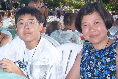 An Asian mother and teen smile at the camera, sitting at an outdoor restaurant.