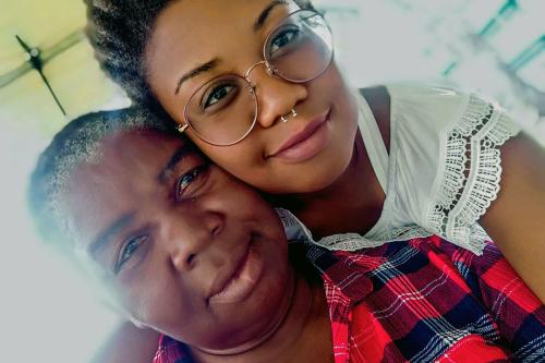 Selfie of mother, in plaid red shirt, and daughter, in white blouse and glasses, both smiling softly.