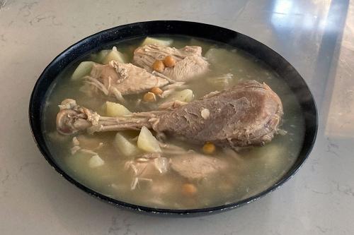 A black bowl full of soup, containing broth, vegetables, and a turkey leg.