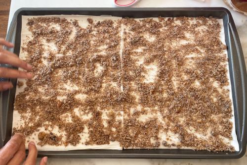 The phyllo dough is now spread with a crumbly brown filling. Two hands pat down the mixture.