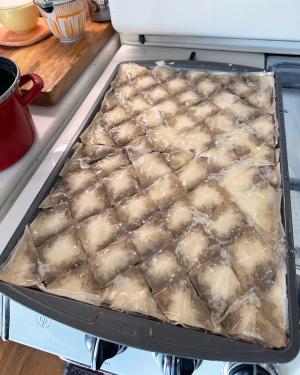 The uncooked baklava, cut into diamond-shaped pieces, now has a white glaze on top.