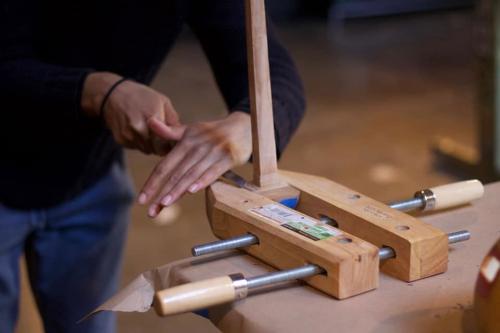 Close-up on a pair of hands chiseling at a piece of wood secured in a vice grip.
