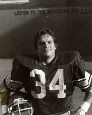 College football player, number 34, poses holding his helmet. Black-and-white photo.