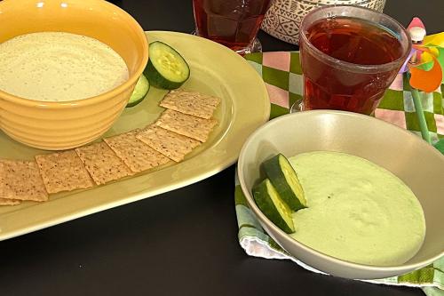 Close-up on two bowls of dip set on a table with slices of cucumbers and crackers. 