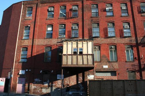 Exterior of four-story apartment building, with a temporary structure protruding from the second story, like a one-room addition.