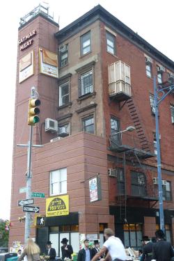 A temporary structure built on a fire escape of a five-story building. On the ground, people walk and bike by.