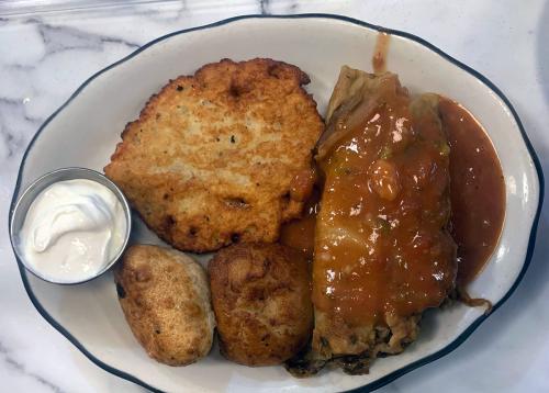 A plate of food: a browned latke, a side of sour cream, two roundish dumplings, and two cabbage rolls smothered in red sauce.