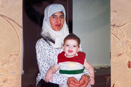 A photograph on top of a pink floral fabric, showing a woman holding a toddler in a red, white, and green sweater in her lap.