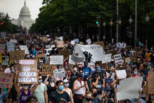 A group of people march down Pennsylvania Avenue in D.C., with the Capitol building in the background. Signs read LISTEN TO BLACK PEOPLE, BLACK LIVES MATTER, DEFUND POLICE, and more out of focus.