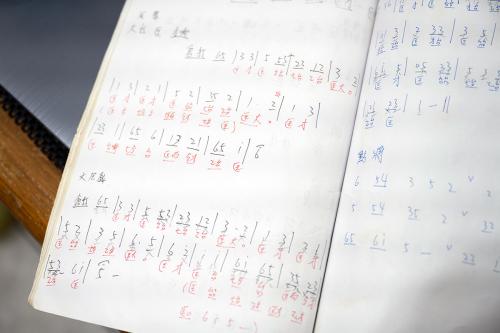 Closeup on a white notebook filled with handwritten sheet music, using Chinese characters. 
