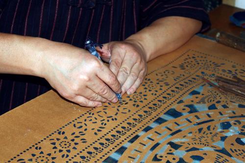 Close-up on two hands carving a pattern into a thick paper stencil. 