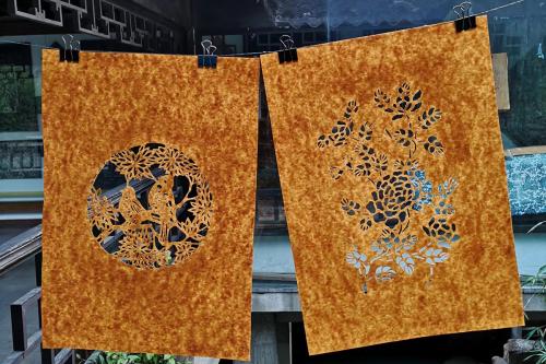 Two finished stencils hanging outside on a clothesline. The carved patterns show birds and flowers.