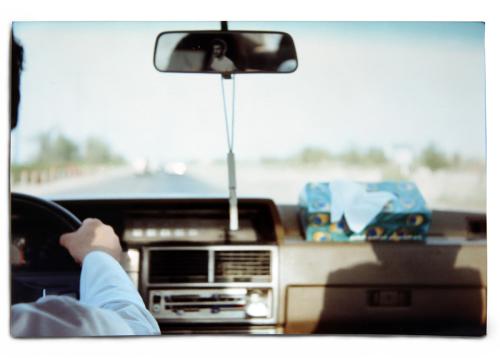 Interior of a car on the road, the driver cut just out of frame. Old color photo.