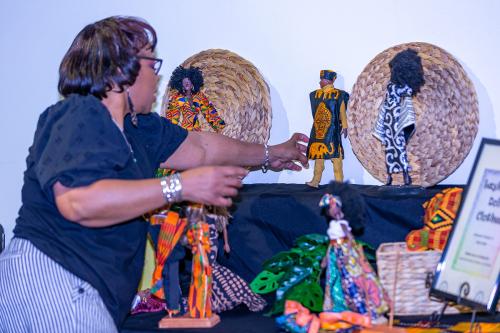 A woman sets up a display of dark-skinned dolls in African prints.