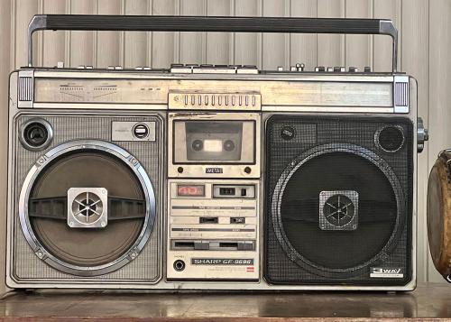 A hand opens the cassette deck of a silver 1980s boombox.