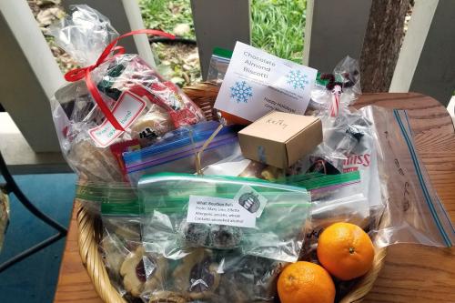 Closeup on a basket assembled with several baggies of cookies and treats, one small cardboard box, and two mandarins.