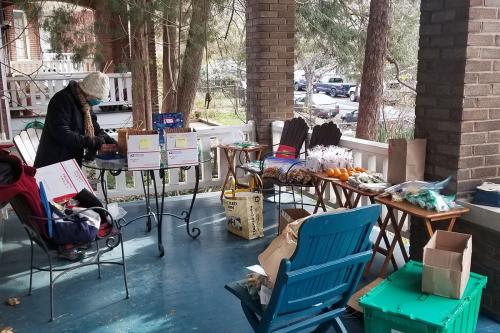 A large front porch is set up with a ring of tables and chairs, full of homemade packages of cookies and other treats. 