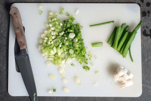 Closeup of cutting board with chopped green onions and knife.