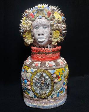 Sculpture of a head with white face with brown line drawings, spiked crown, and mosaic jug-like base.