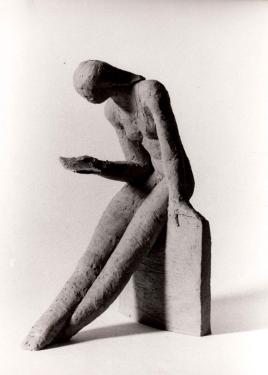 A small stone sculpture of a woman sitting, reading a book.