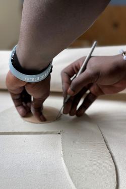 Close-up of the same pair of hands cutting out a circle from the same slab of clay.