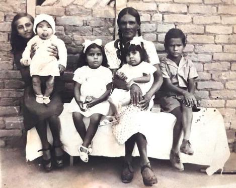 A woman sits with five children, including a baby, all dressed in fine clothes, in front of a brick wall. Black-and-white photo.