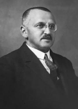 Black-and-white photo of a man in a dark suit, glasses, and trim mustache.